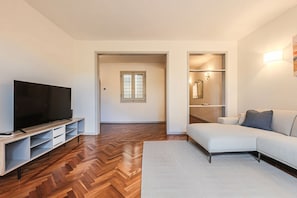 A modern living room with a flat-screen TV, a sofa, and a herringbone-patterned wooden floor.
