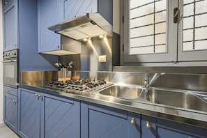 A modern kitchen with blue cabinets, stainless steel appliances, and a large window with a grid pattern.