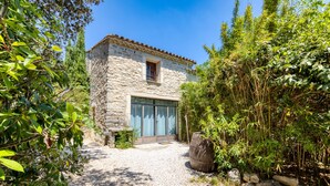 A stone building with a tiled roof, a wooden barrel, and a gravel path. - Holiday Home 'Mas Grand Bosc' with Shared Pool, Private Terrace and Wi-Fi (Notre-Dame-de-Londres)