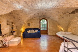 A rustic stone room with a bed, a sofa, and a television.