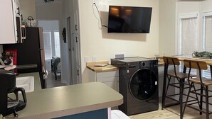 Una cocina moderna con lavadora y secadora integradas, un televisor de pantalla plana montado sobre la encimera y una zona de comedor con sillas de madera.