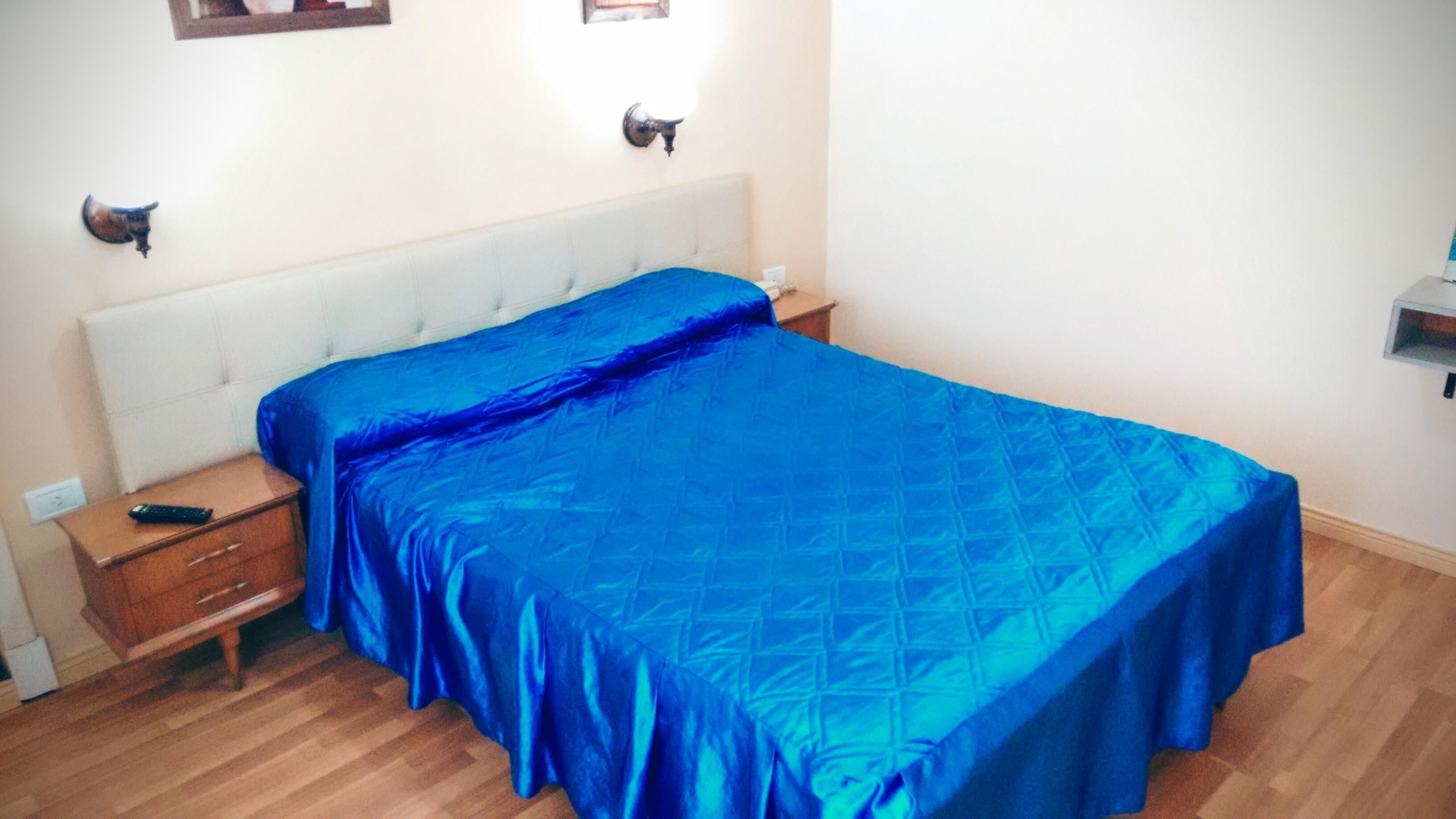 A bedroom with a bed, a nightstand, a dresser, and a wall-mounted lamp.
