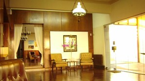 A spacious lobby with a wooden floor, leather armchairs, a chandelier, and a framed picture on the wall. - Acapulco (Necochea)