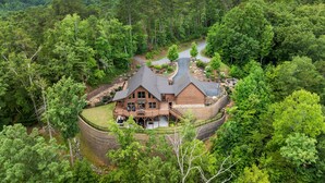 Une grande cabane rustique, entourée d’une forêt dense, avec une allée sinueuse menant à l’entrée.