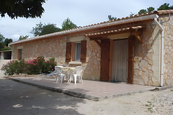 A stone building with a tiled roof, a patio with chairs, and a door.