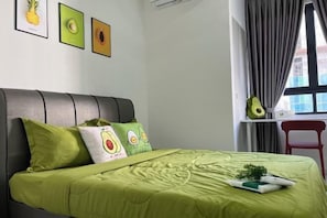 Une chambre avec une couvre-lit verte, une tête de lit et des coussins ornés de motifs d’avocats. Des tableaux encadrés sont accrochés au mur et une décoration en forme d’avocat est posée sur le rebord de la fenêtre.
