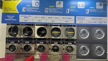 A laundry facility with multiple washing machines and dryers, price list, and instructions.