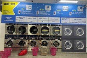 Een wasserette met meerdere wasmachines en drogers, een prijslijst en instructies.