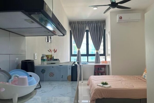 A compact hotel room with a kitchenette, a bed with a pink bedspread, a ceiling fan, and a window with curtains. - C&Y Horizon Suites Homestay Sepang - KLIA Transit - Near XiaMen University (Sepang)