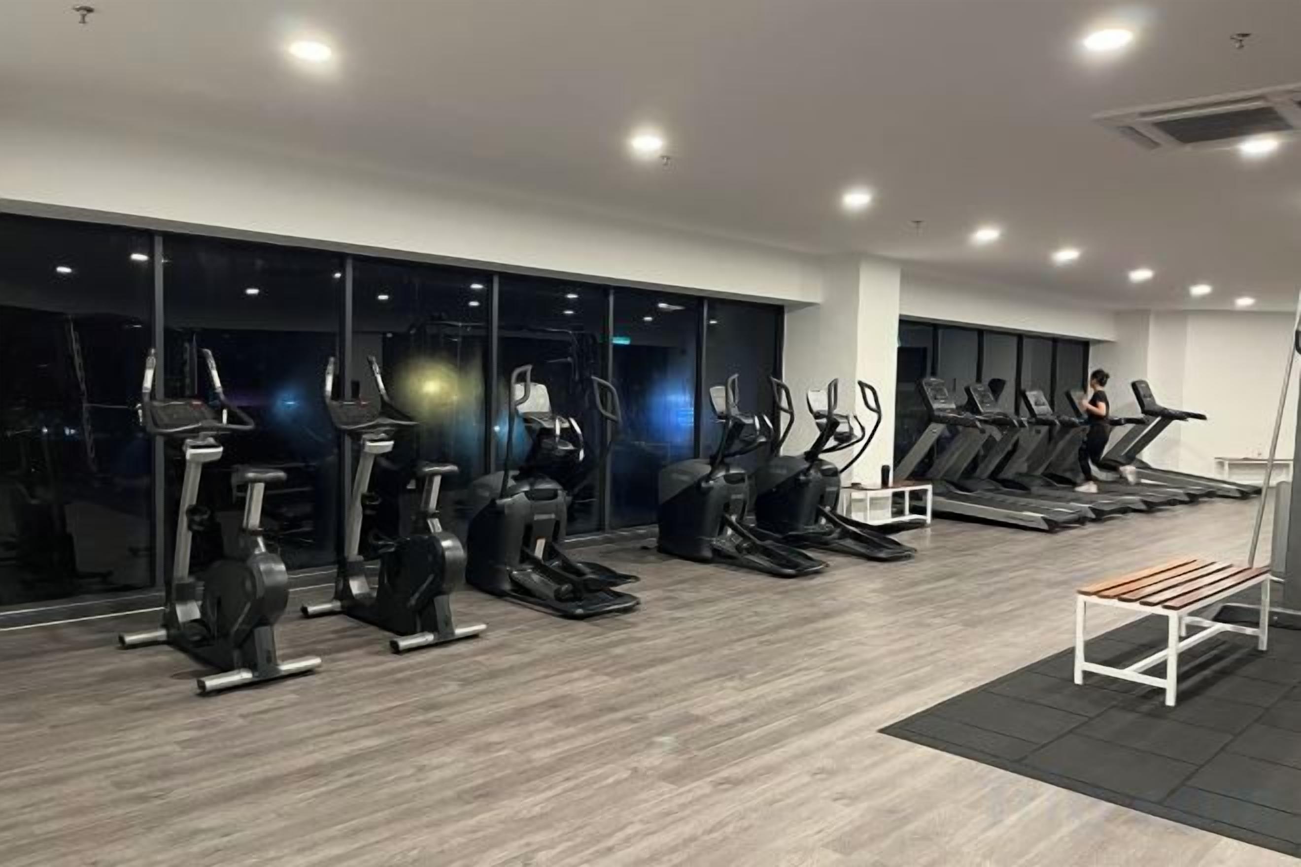 A gym with various exercise equipment, including treadmills and stationary bikes, and large windows.