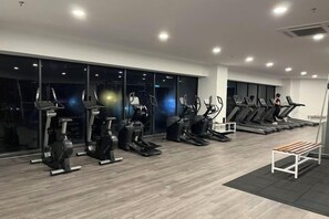 Un gimnasio con equipos de ejercicio variados, incluyendo cintas de correr y bicicletas estáticas, y grandes ventanales.