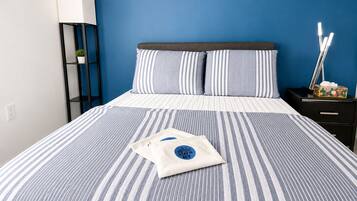 A bed with striped bedding, a pillow with a logo, a bedside table with a lamp, and a nightstand with a tissue box.