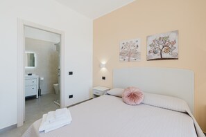 Une chambre à coucher comprenant un lit, une table de chevet, une lampe fixée au mur et deux œuvres d’art décoratives.
