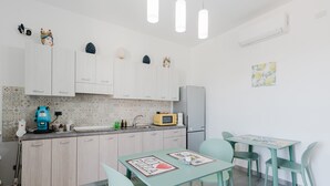 Une cuisine compacte avec des meubles blancs, un four à micro-ondes et une machine à café. On y trouve deux tables avec des chaises, ainsi qu’un petit réfrigérateur.