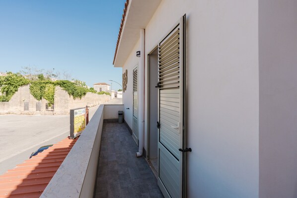 A narrow outdoor corridor with a tiled floor, a closed shutter door, and a small trash bin.