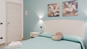Une chambre à coucher comprenant un lit, une table de chevet, une lampe fixée au mur et deux œuvres d’art murales.