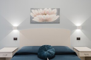 Une chambre à coucher avec un lit, un oreiller, une table de chevet, une lampe fixée au mur et un tableau.