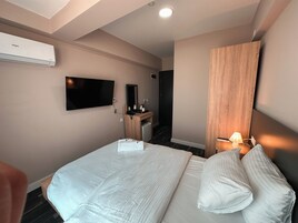 Una habitación de hotel con una cama, un escritorio con una computadora, un televisor montado en la pared y un equipo de aire acondicionado.