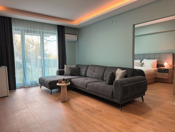 Una sala de estar moderna con un sofá gris, una mesita redonda y una mesita de noche con una lámpara.