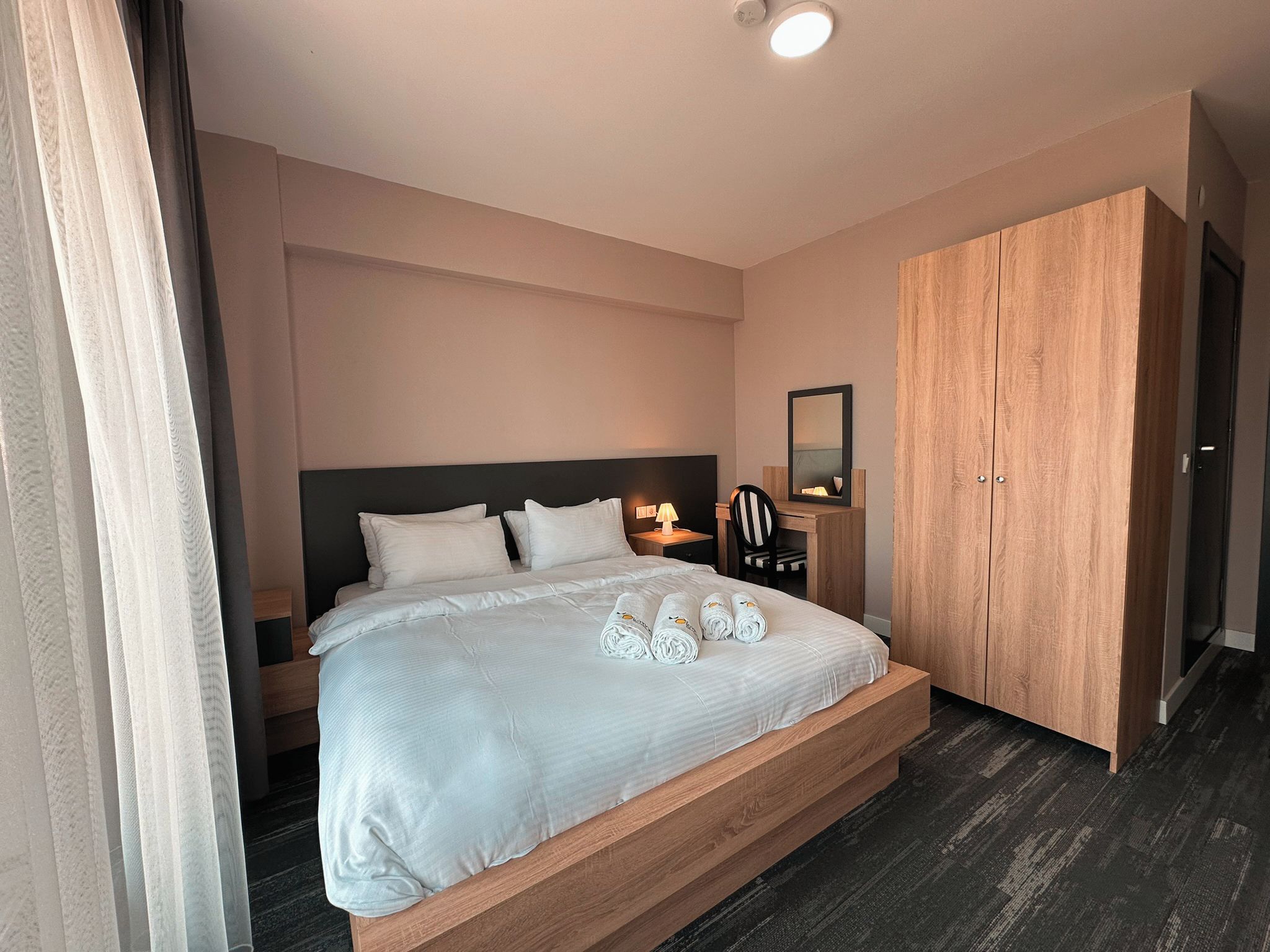 Quarto de hotel com cama, mesa de cabeceira, luminária, espelho e guarda-roupa.