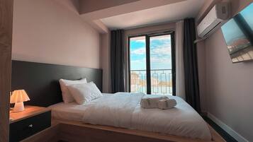 A hotel room with a bed, a nightstand, a lamp, a window with curtains, and an air conditioning unit.