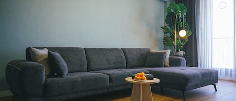 A modern living room with a grey sofa, a round wooden coffee table, and a large green plant.