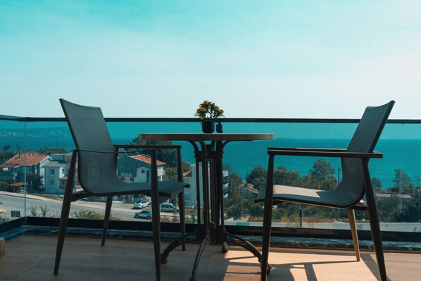 A balcony with two chairs and a table, overlooking a coastal view.