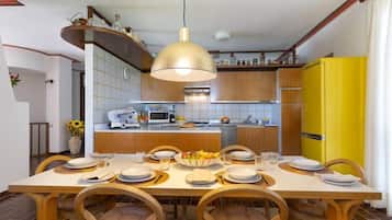 A dining area with a wooden table set for six, a yellow refrigerator, and a kitchen in the background.