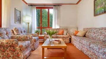 A living room with floral-patterned sofas, a wooden coffee table, and a window with curtains.