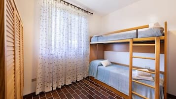 A bunk bed room with a wooden ladder, a window with floral curtains, and a tiled floor.