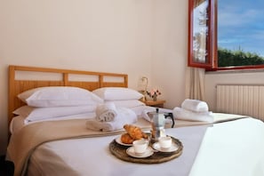 A neatly made bed with white linens, a tray with croissants and coffee cups, and a view of greenery through a window. - Lesa Villas (Lesa)