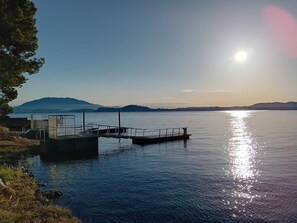 A calm lake with a dock extending into the water, surrounded by hills and trees. - Lesa Villas (Lesa)