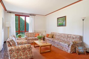 Un salon avec des canapés à motifs floraux, une table basse en bois et une grande fenêtre avec des rideaux.