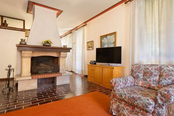 A living room with a fireplace, a sofa, a television, and a wooden cabinet. - Lesa Villas (Lesa)