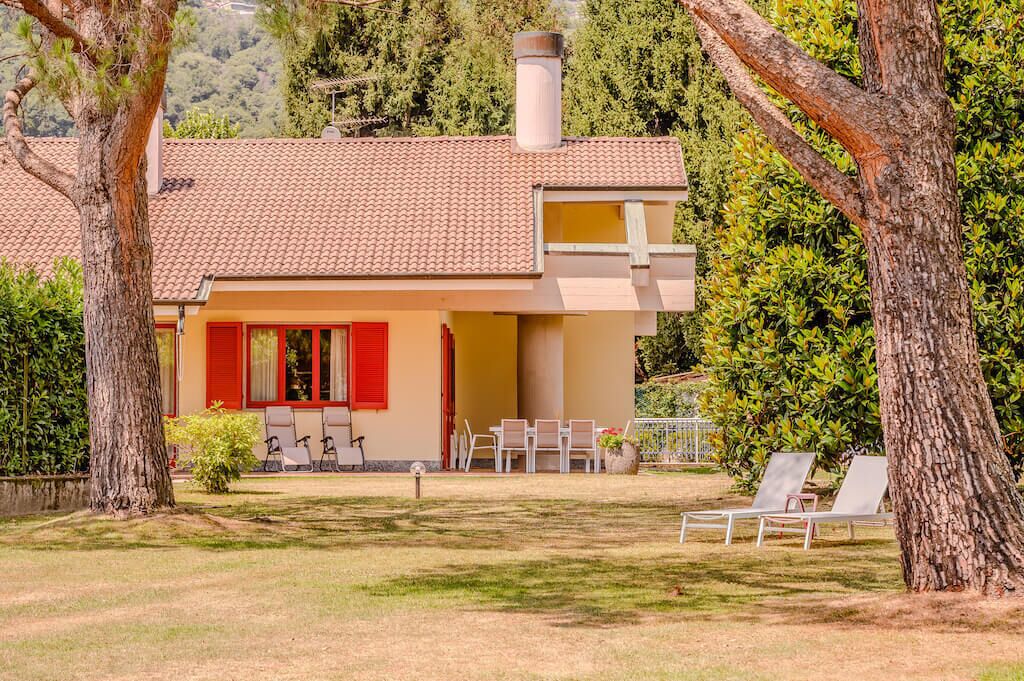 Une maison avec un toit en tuiles, un balcon et un jardin agrémenté de chaises et d’une table.