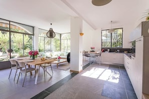 A modern kitchen with large windows, a dining area with a wooden table and chairs, and a kitchen island. - Villa Lesa (Lesa)