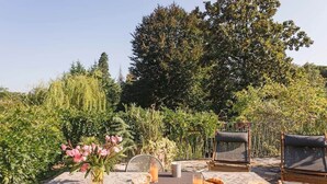 An outdoor dining area with a table set for two, surrounded by lush greenery and trees. - Villa Lesa (Lesa)