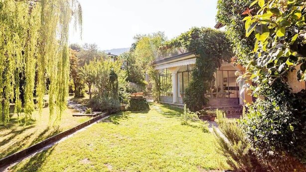 A well-maintained garden with a pathway leading to a building with large windows. - Villa Lesa (Lesa)