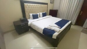 Una cama bien tendida con ropa de cama azul y blanca, un cabecero oscuro y una mesita de noche con una lámpara.