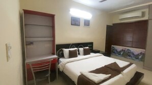 Habitación de hotel con cama, escritorio, silla, televisor y aire acondicionado.