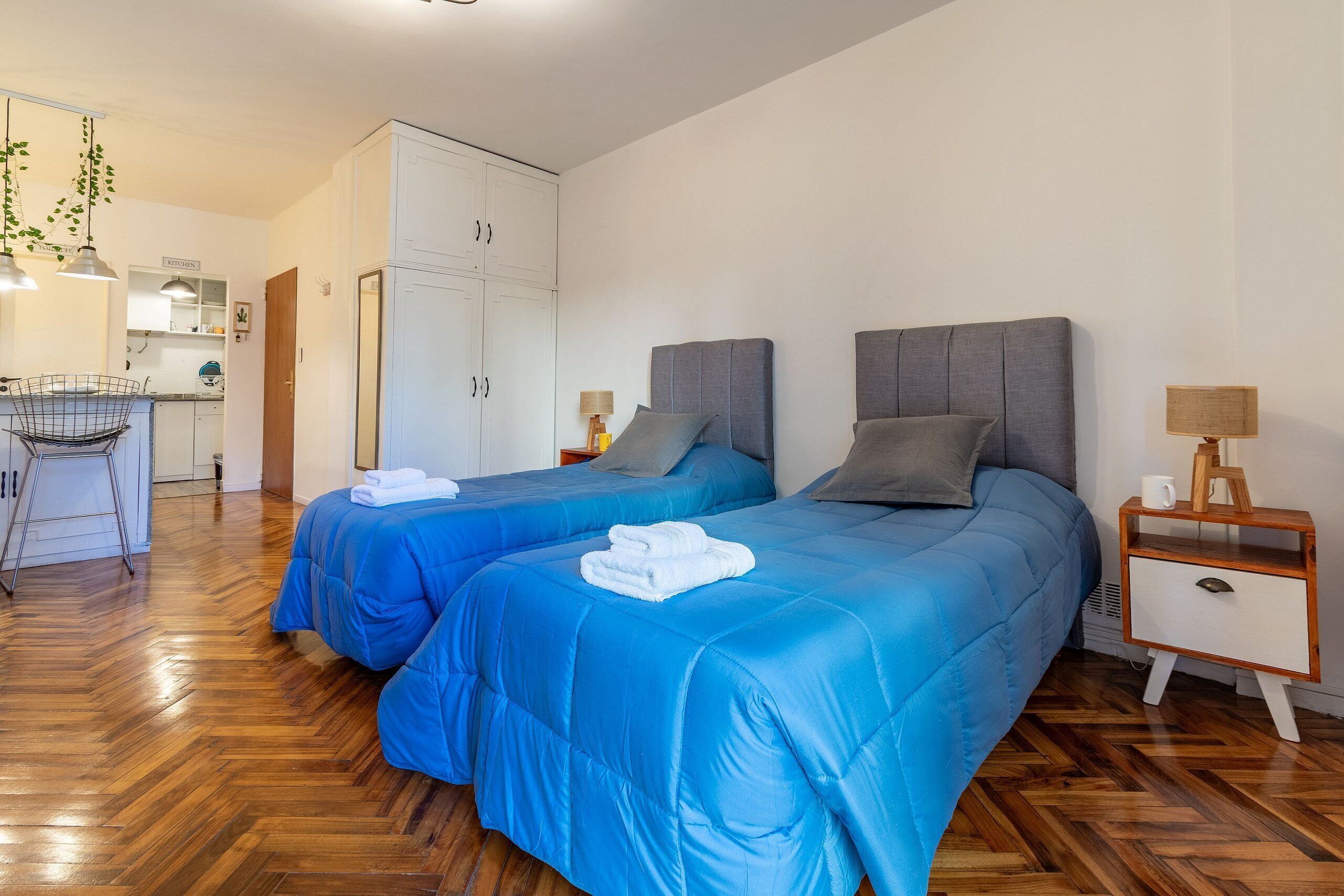 Quarto de hotel com duas camas, piso de madeira, cozinha compacta e pequena sala de jantar.
