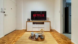 Een moderne woonkamer met een houten vloer, een aan de muur bevestigde televisie en een klein tafeltje met kopjes en een glas.