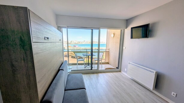 Un apartamento moderno con un balcón amplio, un sofá y un televisor montado en la pared.