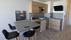 Cocina moderna con armarios de madera, microondas integrado y refrigerador pequeño. Hay un rincón con taburetes y una mesa, y un cuadro de un faro se ve en la pared.