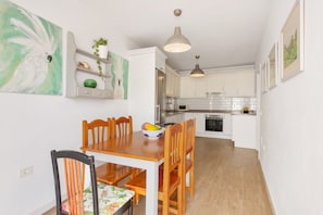 A dining area with a wooden table and chairs, a bowl of fruit, and a painting on the wall.