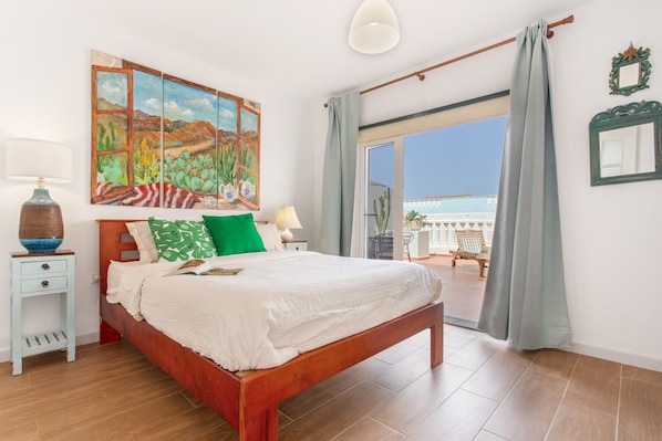 A bedroom with a bed, a nightstand, a painting, and a view through a sliding door.
