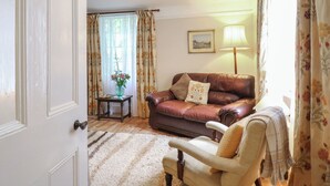 Ett mysigt vardagsrum med en brun lädersoffa, en trästol, ett litet bord med en vas och en lampa.