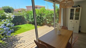 Eine Holzterrasse mit Tisch und Stühlen, ein Korbstuhl, ein weißes Schranksystem und eine hängende Weidenleuchte.