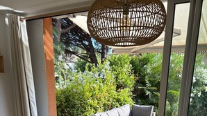 Ein Essbereich mit einem Tisch, der für vier Personen gedeckt ist, umgeben von Korbstühlen, einer Canapésgarnitur und einem großen Fenster mit Blick auf einen Garten.
