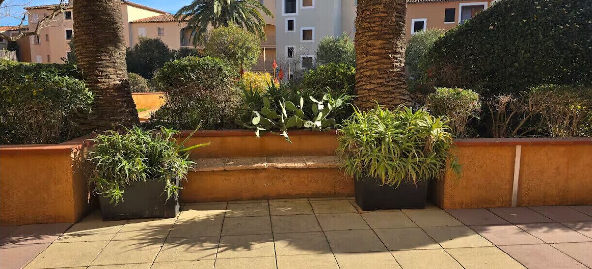Une terrasse sur le toit agrémentée de plantes en pot, dotée d’un sol carrelé et offrant une vue sur les immeubles d’habitation en arrière-plan.